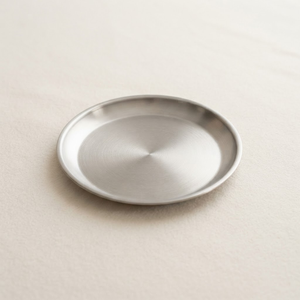 Small brushed stainless steel side plate on a warm off-white background